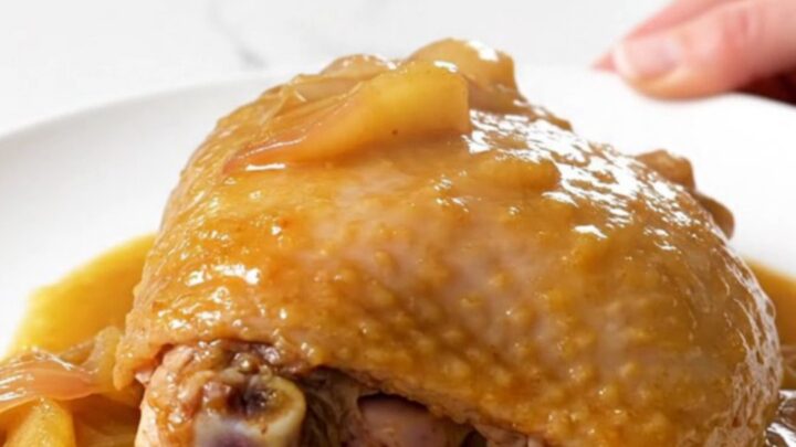 Close up of a tender braised turkey thigh in a rich apple Dijon sauce on a white plate.