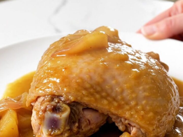 Close up of a tender braised turkey thigh in a rich apple Dijon sauce on a white plate.