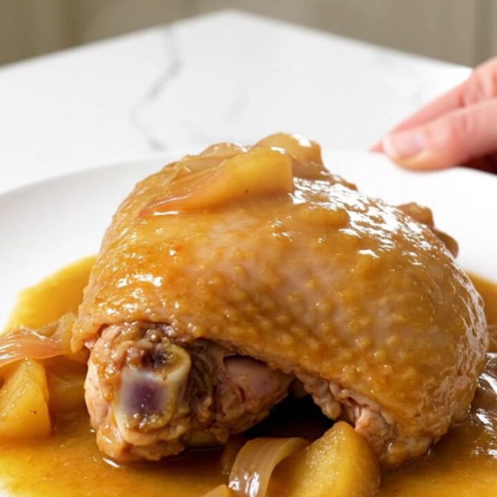 Close up of a tender braised turkey thigh in a rich apple Dijon sauce on a white plate.