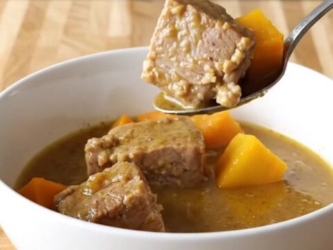 A close-up of a steaming bowl of pork and butternut squash stew with visible chunks of tender meat.
