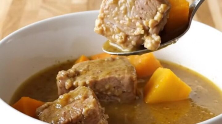A close-up of a steaming bowl of pork and butternut squash stew with visible chunks of tender meat.