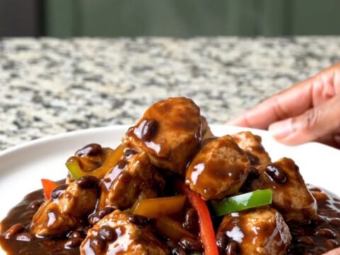 A top-down view of slow cooker black bean sauce chicken with peppers and ginger in a black ceramic slow cooker.