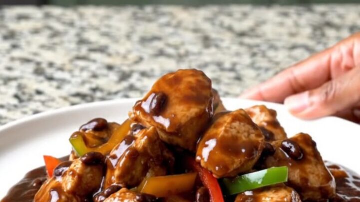 A top-down view of slow cooker black bean sauce chicken with peppers and ginger in a black ceramic slow cooker.