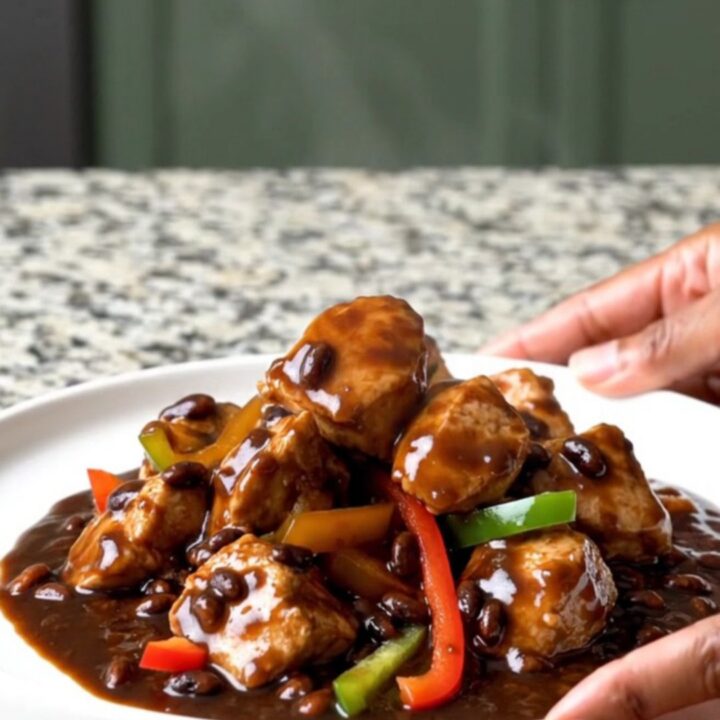 A top-down view of slow cooker black bean sauce chicken with peppers and ginger in a black ceramic slow cooker.