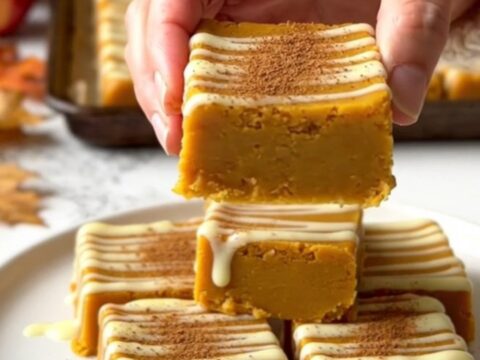 A top-down view of rows of orange pumpkin fudge squares on a parchment-lined baking sheet.