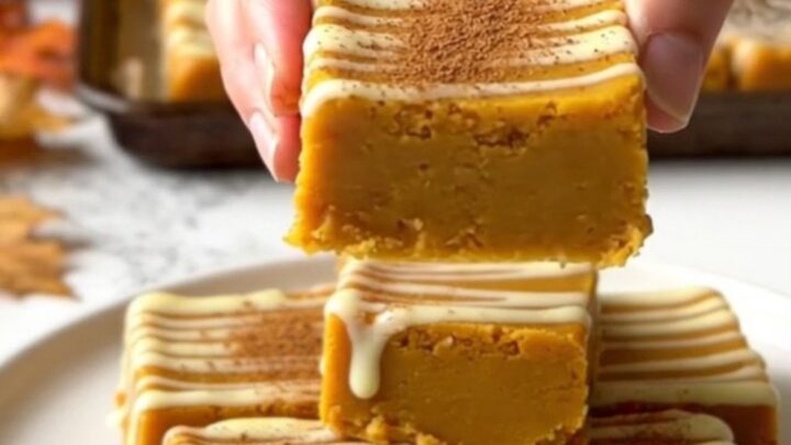 A top-down view of rows of orange pumpkin fudge squares on a parchment-lined baking sheet.
