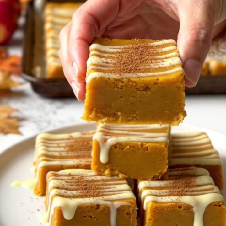 A top-down view of rows of orange pumpkin fudge squares on a parchment-lined baking sheet.