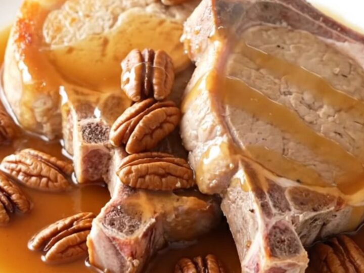 A close-up of tender boneless pork chops glazed in a rich maple butter sauce with scattered pecans in a slow cooker.
