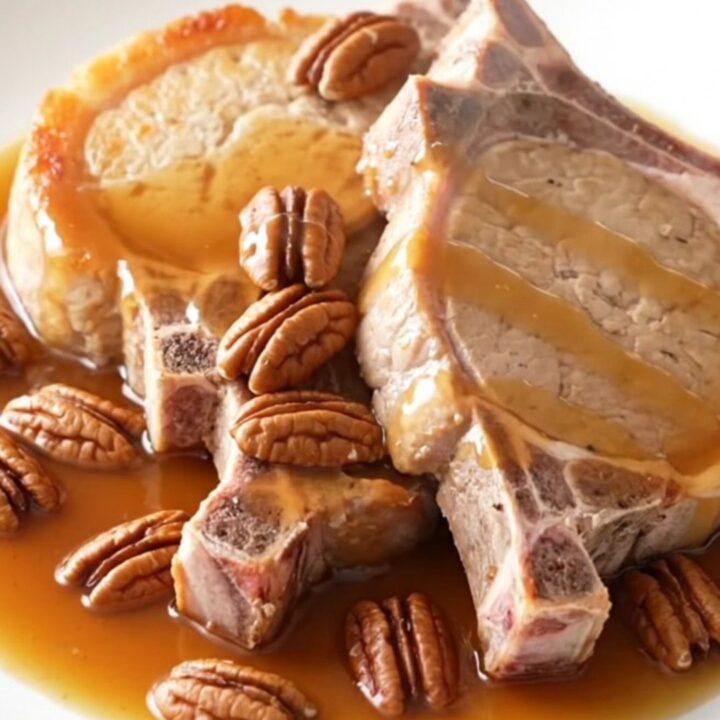 A close-up of tender boneless pork chops glazed in a rich maple butter sauce with scattered pecans in a slow cooker.
