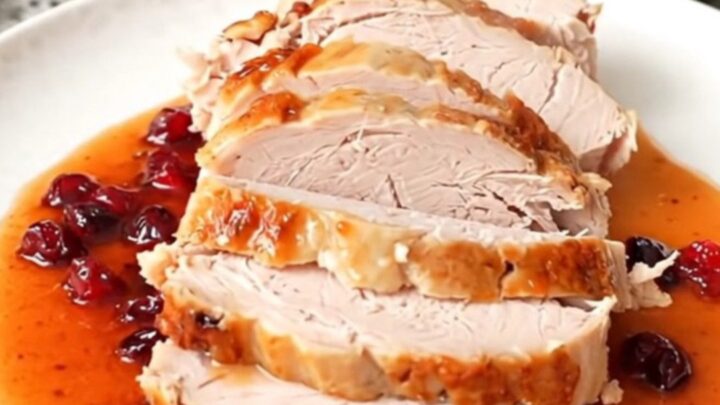 A sliced turkey breast coated in a glossy, dark red cranberry hot honey sauce on a white plate.