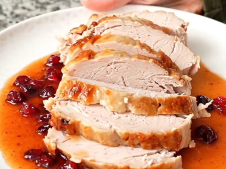 A sliced turkey breast coated in a glossy, dark red cranberry hot honey sauce on a white plate.