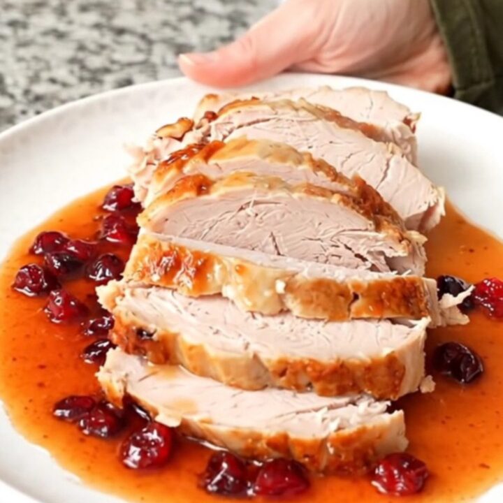 A sliced turkey breast coated in a glossy, dark red cranberry hot honey sauce on a white plate.