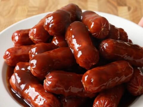 A stainless steel slow cooker filled with glazed mini smoked sausages in a sweet root beer barbecue sauce.
