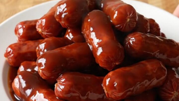 A stainless steel slow cooker filled with glazed mini smoked sausages in a sweet root beer barbecue sauce.