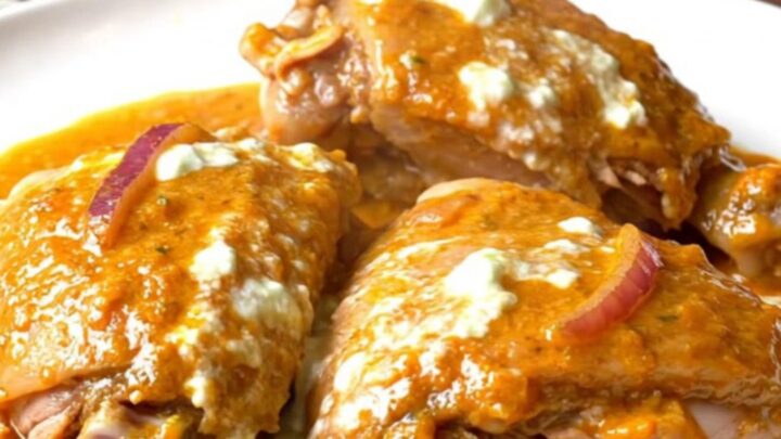 A close-up of slow-cooked tandoori turkey thighs with a vibrant, spiced yogurt sauce and softened red onions.