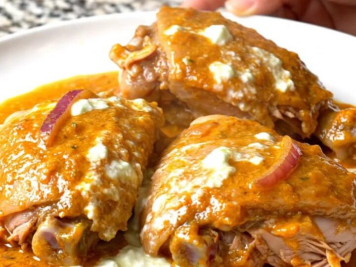 A close-up of slow-cooked tandoori turkey thighs with a vibrant, spiced yogurt sauce and softened red onions.