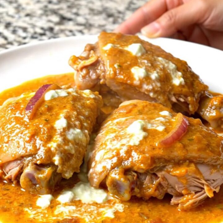 A close-up of slow-cooked tandoori turkey thighs with a vibrant, spiced yogurt sauce and softened red onions.