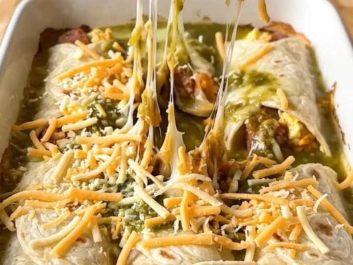 A top-down view of a rectangular baking dish filled with sausage and egg burritos covered in salsa verde and melted pepper