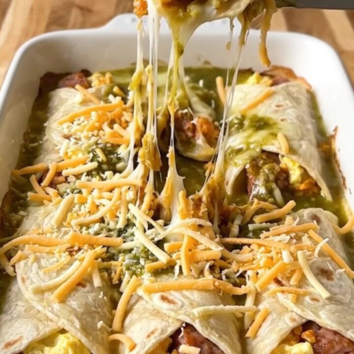 A top-down view of a rectangular baking dish filled with sausage and egg burritos covered in salsa verde and melted pepper