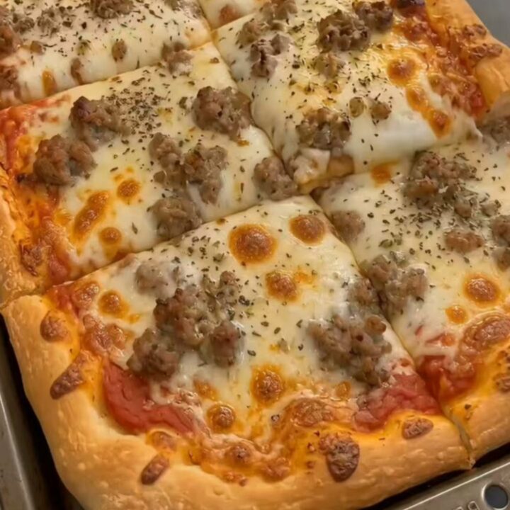 A thick, square slice of sheet pan pizza being lifted with a spatula, showing gooey melted mozzarella and steam.