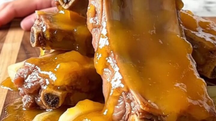 A close-up of slow-cooked, tender pork spareribs coated in a thick, glossy apricot glaze on a wooden board.