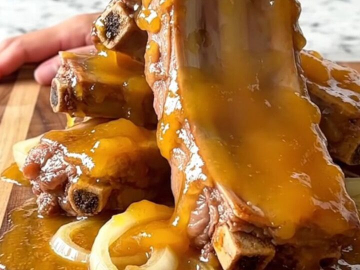 A close-up of slow-cooked, tender pork spareribs coated in a thick, glossy apricot glaze on a wooden board.