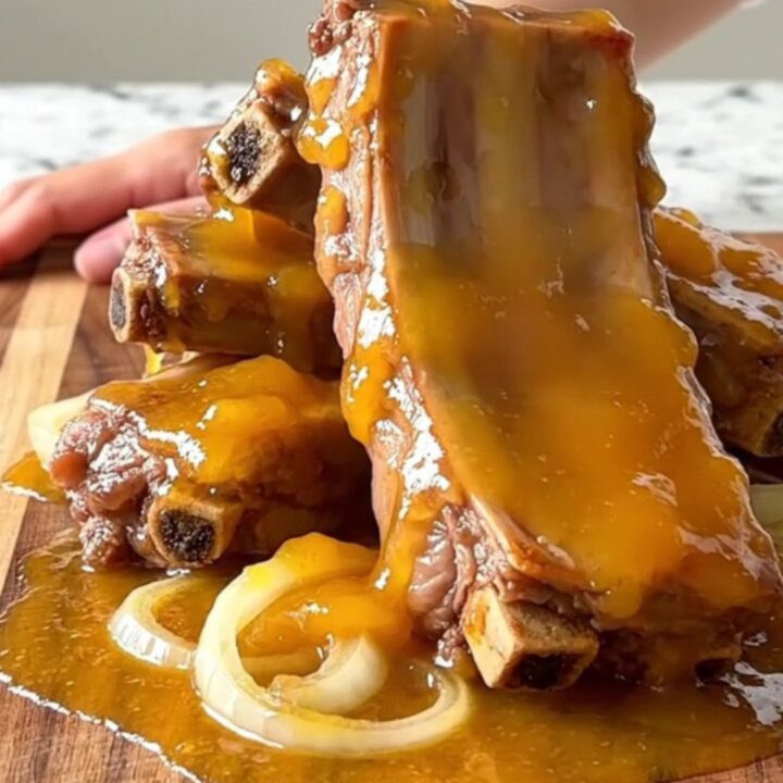 A close-up of slow-cooked, tender pork spareribs coated in a thick, glossy apricot glaze on a wooden board.