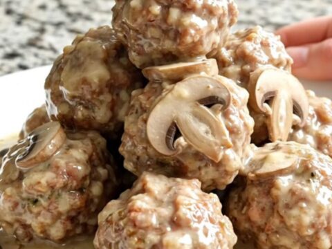 A close-up of tender meatballs smothered in a creamy mushroom and Swiss cheese sauce in a slow cooker.