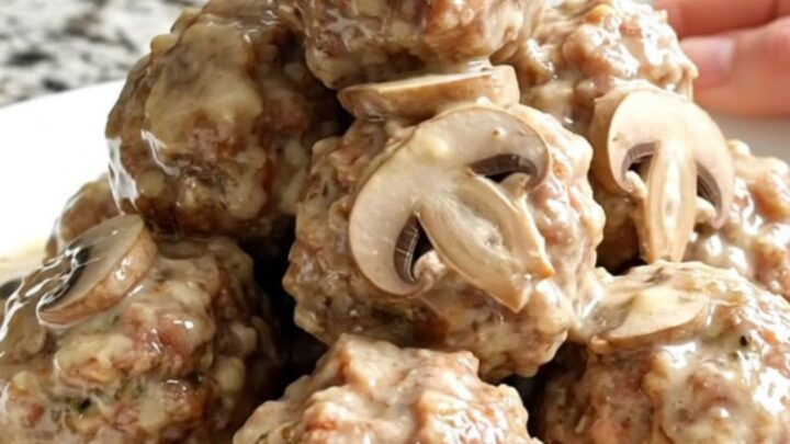 A close-up of tender meatballs smothered in a creamy mushroom and Swiss cheese sauce in a slow cooker.