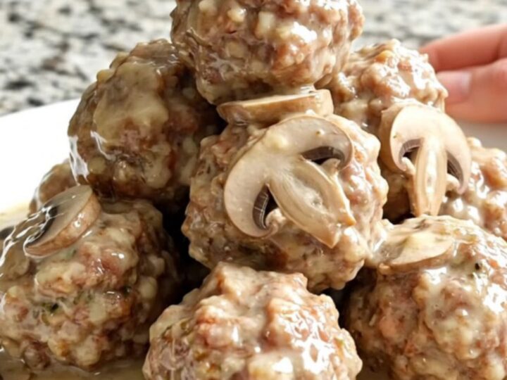 A close-up of tender meatballs smothered in a creamy mushroom and Swiss cheese sauce in a slow cooker.