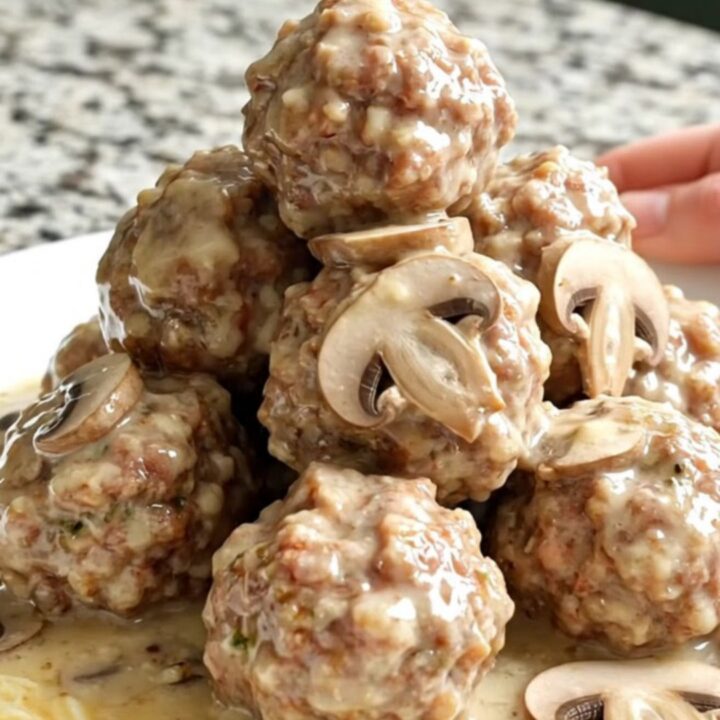 A close-up of tender meatballs smothered in a creamy mushroom and Swiss cheese sauce in a slow cooker.