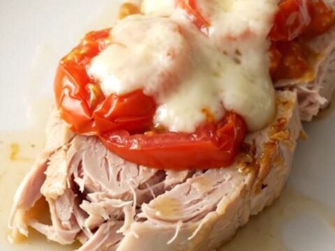 A high-angle shot of raw turkey tenderloins in a slow cooker topped with tomatoes, basil, and fresh mozzarella slices.