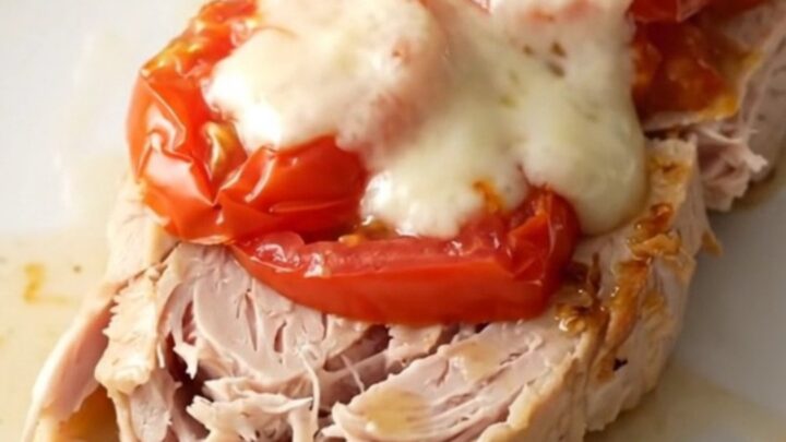 A high-angle shot of raw turkey tenderloins in a slow cooker topped with tomatoes, basil, and fresh mozzarella slices.