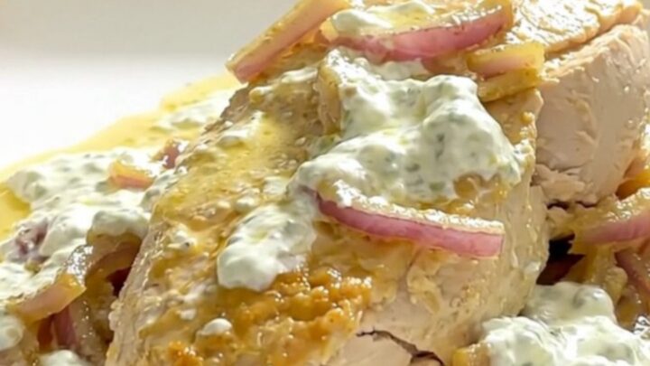 A close-up of tender chicken breast in a creamy lemon yogurt sauce on a white plate.
