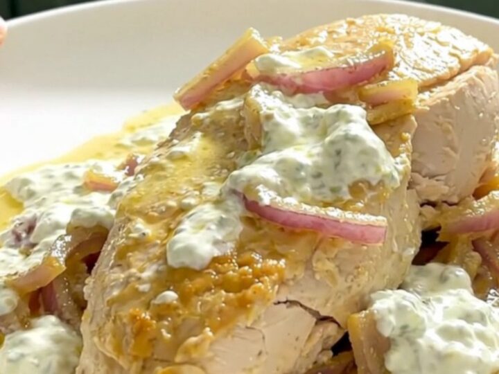A close-up of tender chicken breast in a creamy lemon yogurt sauce on a white plate.