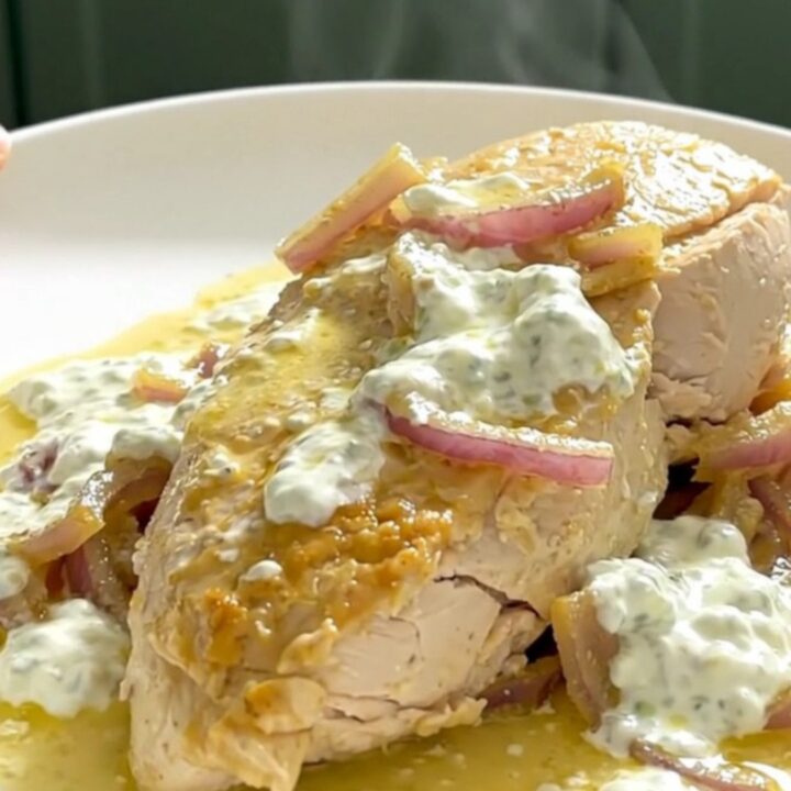 A close-up of tender chicken breast in a creamy lemon yogurt sauce on a white plate.