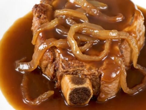 A close-up of tender, slow-cooked bone-in pork steaks covered in a rich brown sugar bourbon sauce with soft onions on a white