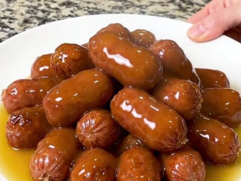 A slow cooker filled with mini smoked sausages and halved baby potatoes in a glossy honey butter sauce.