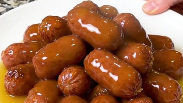 A slow cooker filled with mini smoked sausages and halved baby potatoes in a glossy honey butter sauce.