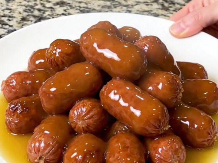 A slow cooker filled with mini smoked sausages and halved baby potatoes in a glossy honey butter sauce.