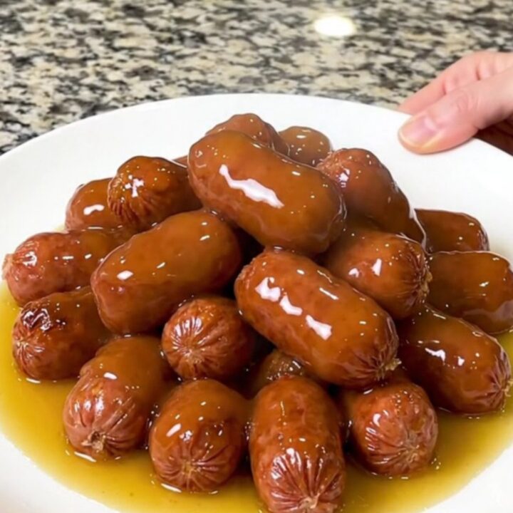 A slow cooker filled with mini smoked sausages and halved baby potatoes in a glossy honey butter sauce.