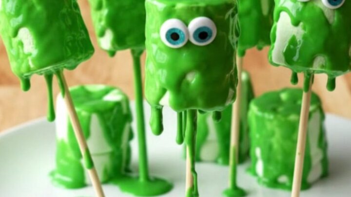 A display of green monster marshmallow pops with candy eyes on a white plate.