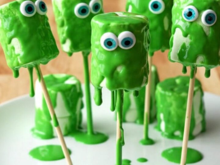 A display of green monster marshmallow pops with candy eyes on a white plate.