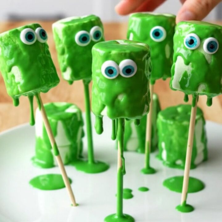 A display of green monster marshmallow pops with candy eyes on a white plate.