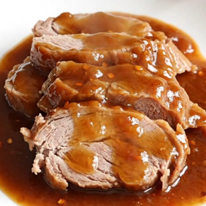 A whole, raw pork tenderloin resting in a slow cooker insert next to a hand adding a second piece.