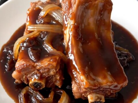 A slow cooker filled with tender, glazed plum spare ribs and sliced onions.