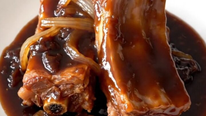 A slow cooker filled with tender, glazed plum spare ribs and sliced onions.