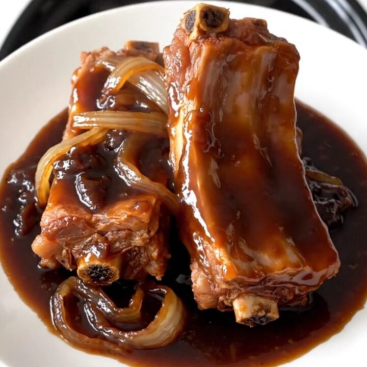 A slow cooker filled with tender, glazed plum spare ribs and sliced onions.