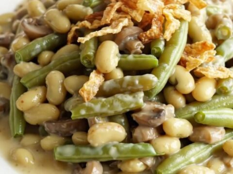 A close-up view of a creamy green bean casserole in a stoneware crock, topped with golden crispy fried onions.