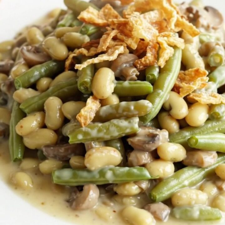 A close-up view of a creamy green bean casserole in a stoneware crock, topped with golden crispy fried onions.
